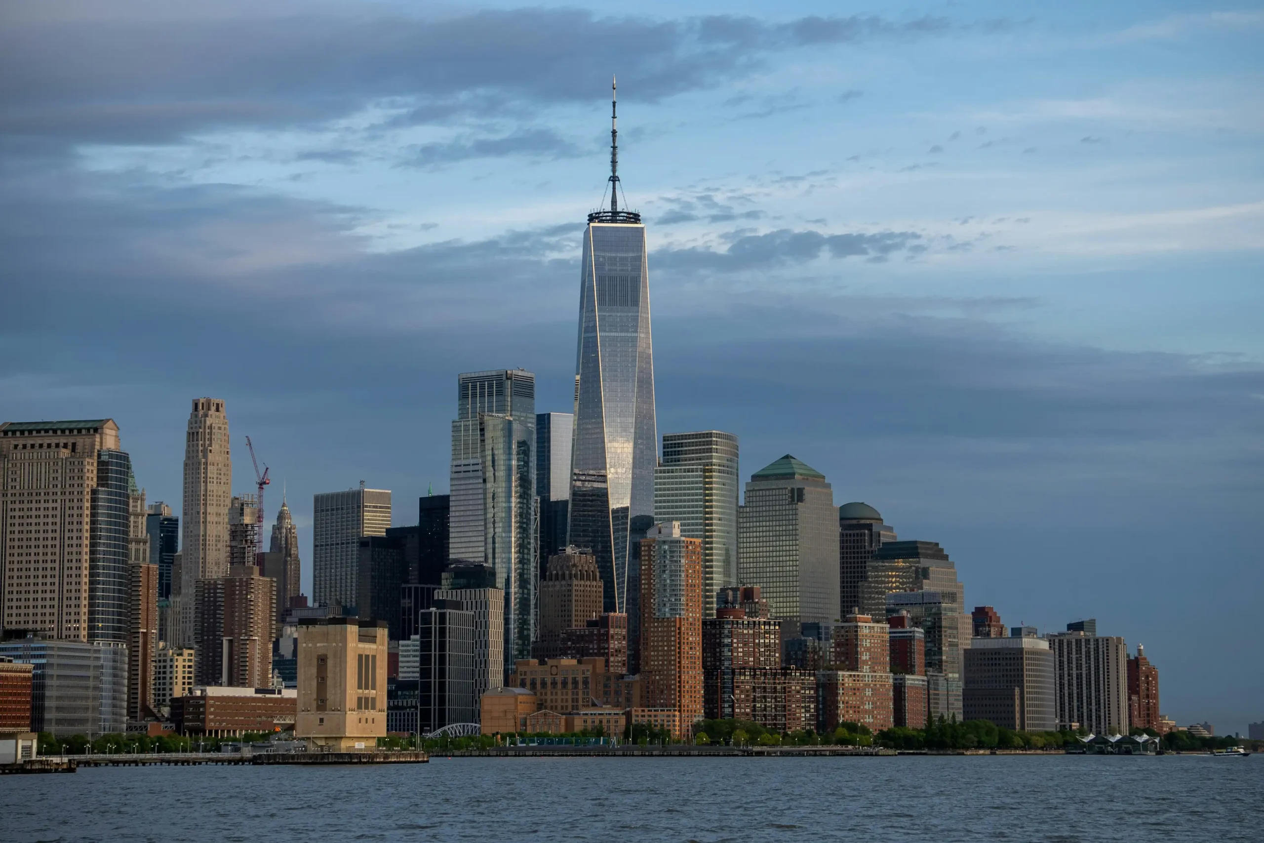One World Trade Center towering over the New York City skyline with various buildings in the foreground and a cloudy sky